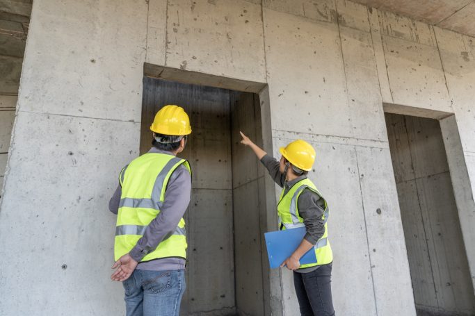 Zwei Bauleiter mit Schutzhelmen überprüfen ein Rohbauprojekt und diskutieren darüber.