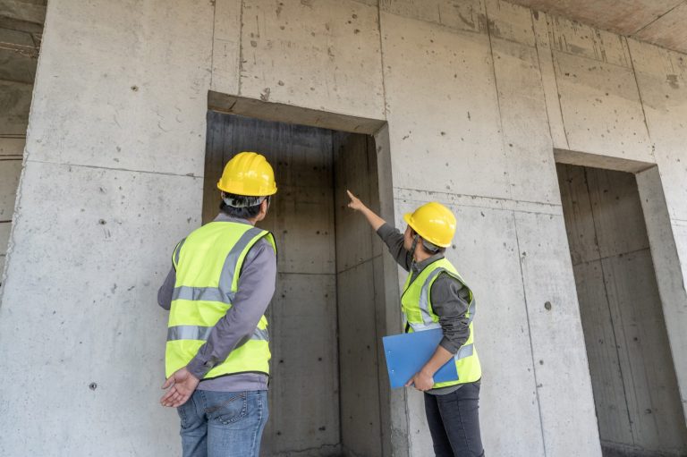 Das Bild zeigt zwei Bauplaner im Gespräch vor einem Aufzugschacht im Rohbau